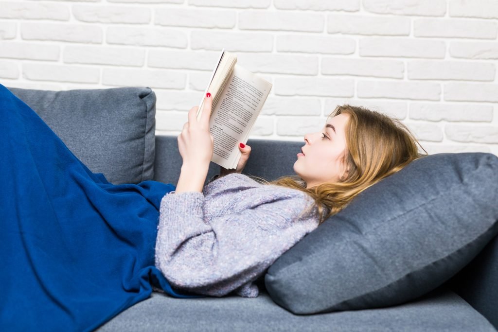 Blonde woman reading a book on her sofa